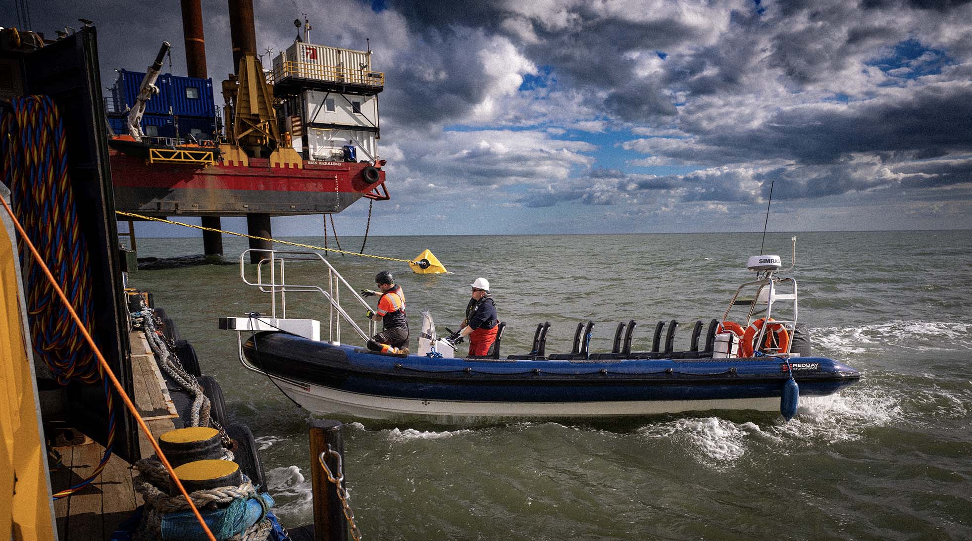 A support boat alongside the offshore work platform beneath a cloud-filled sky