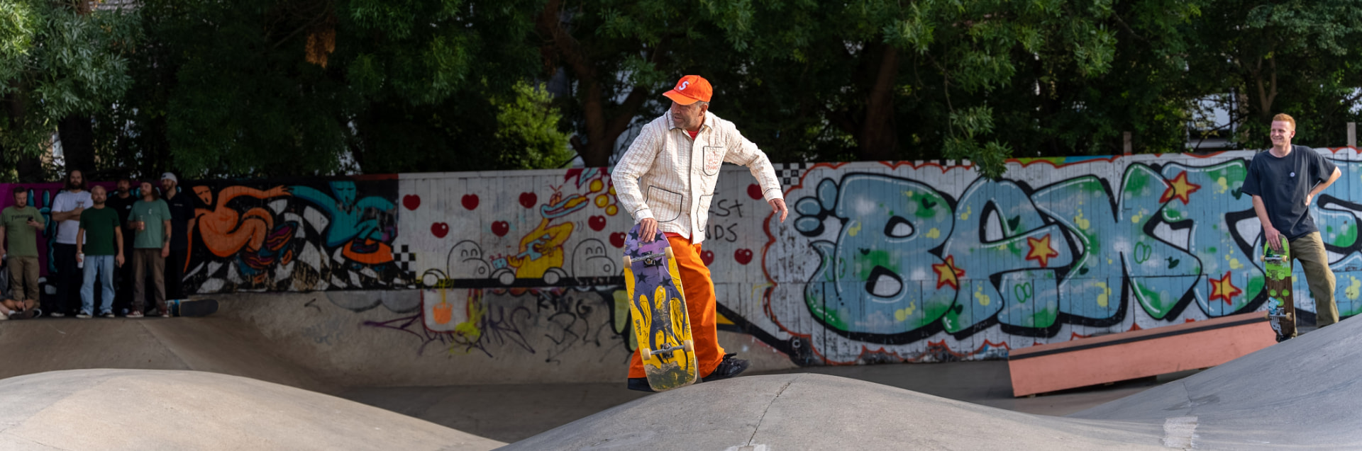 Mark Gonzales riding past the graffiti wall holding his board at his side