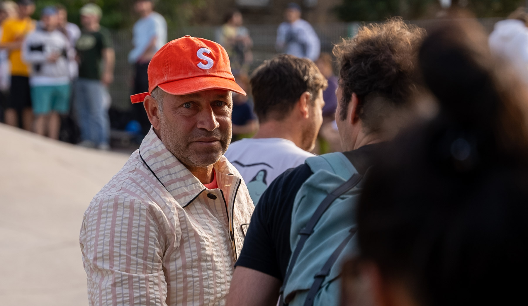 Close portrait of Mark Gonzales in his orange cap amongst the crowd at golden hour