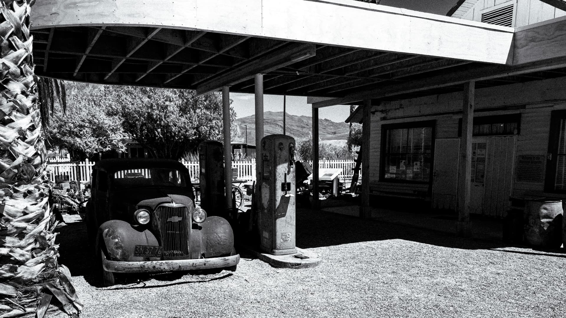 An abandoned car parked under the canopy of an old gas station in the desert