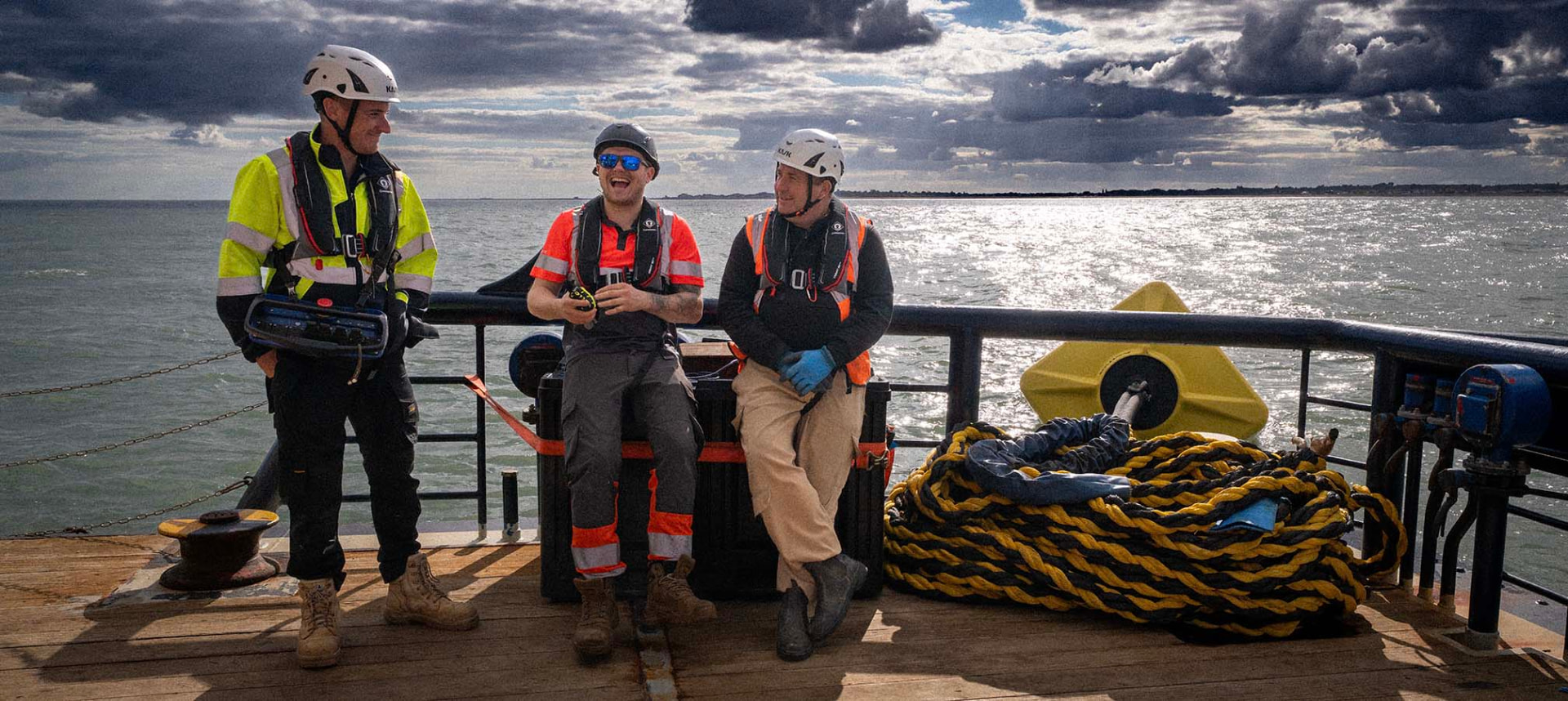 Three crew members sharing a laugh at the stern beside coiled diving umbilicals
