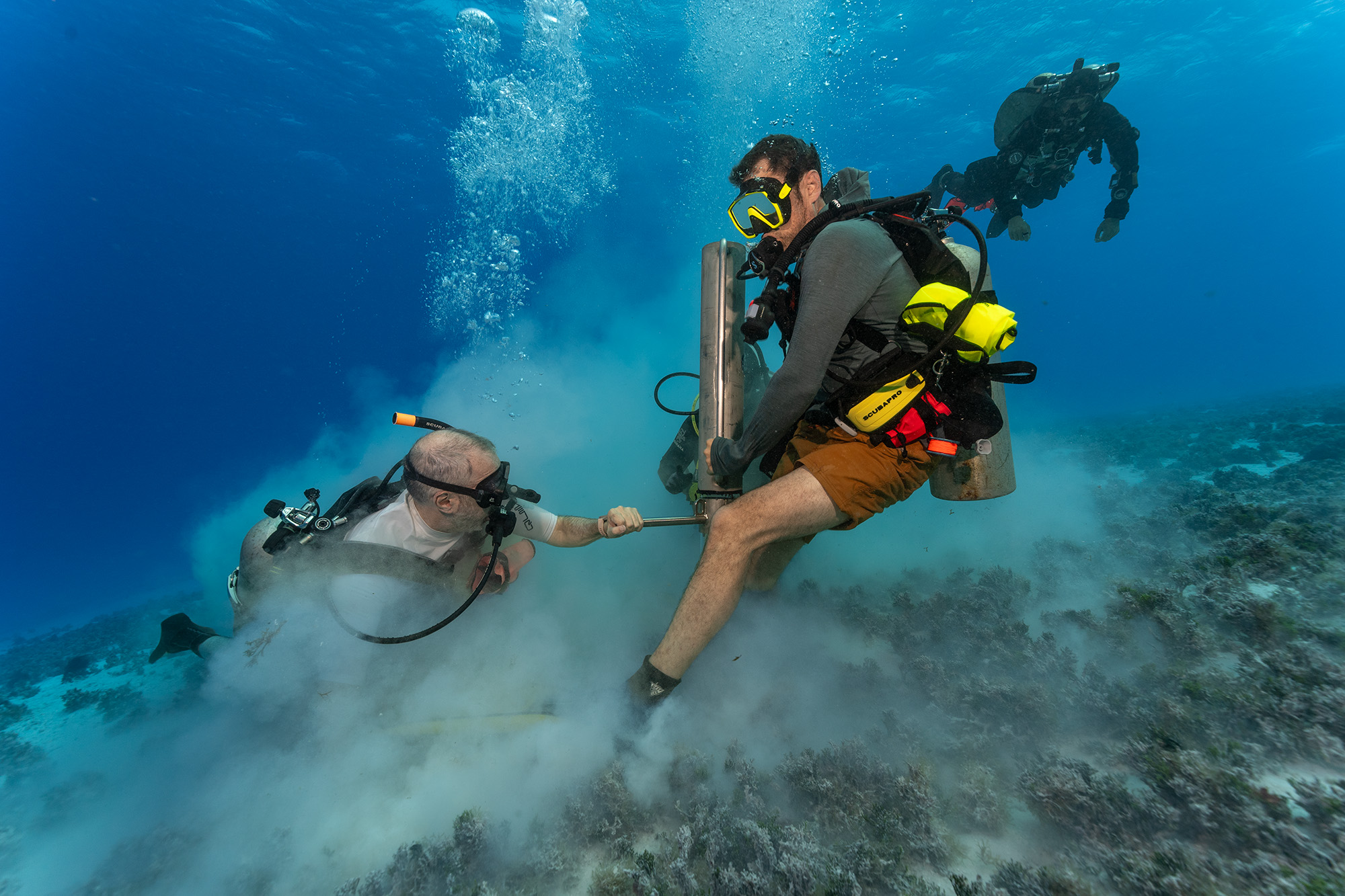 Two divers driving a core tube into the reef floor