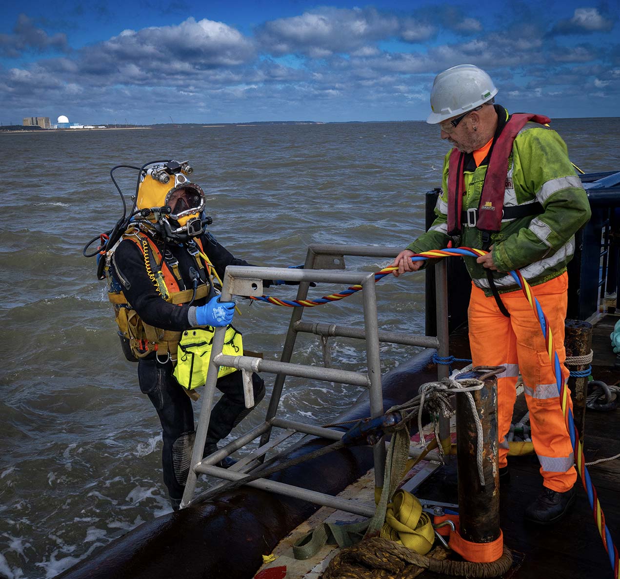 A surface-supplied diver on the boarding ladder with a tender watching his umbilical